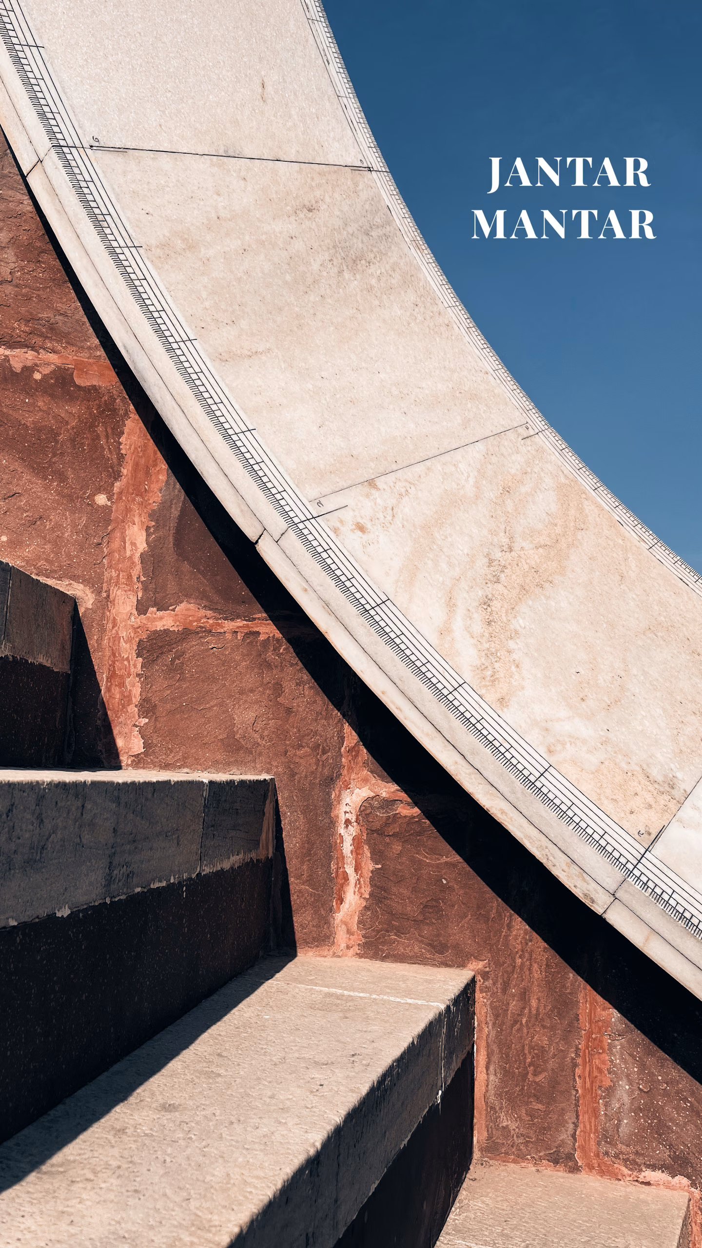 Curved marble scale of a giant sundial with engraved graduation marks, set against red sandstone steps and blue sky