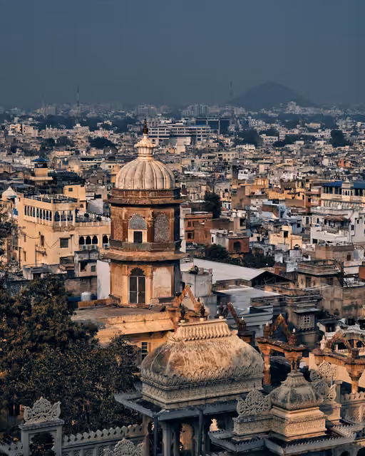 Aerial view of a domed palace tower with ornate carved cupolas in the foreground, overlooking a dense cityscape of rooftops stretching to a hazy hill.