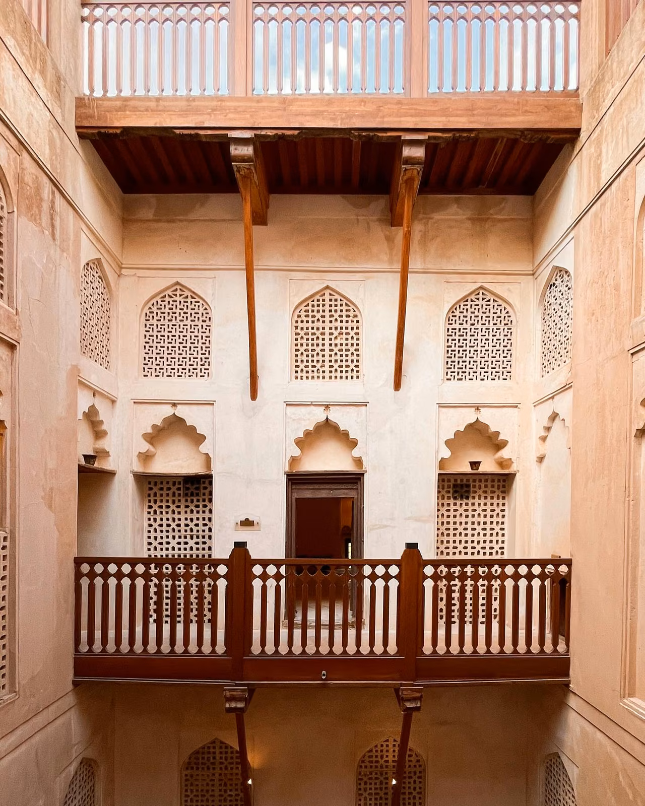Interior courtyard of a traditional fort with carved lattice windows, arched niches, wooden balconies, and diagonal wooden support beams overhead.